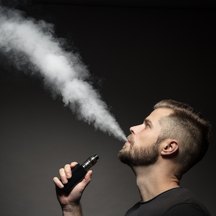 A guy smoking a making a cloud and holding a vape in hand.