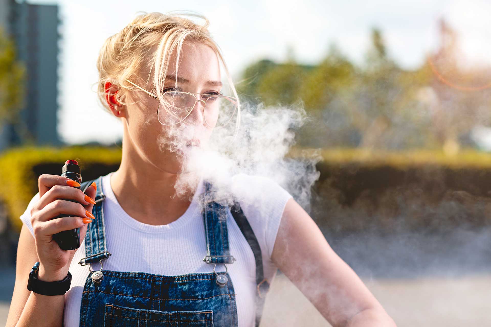 A girl holding a vape with a smoke coming from her mouth.